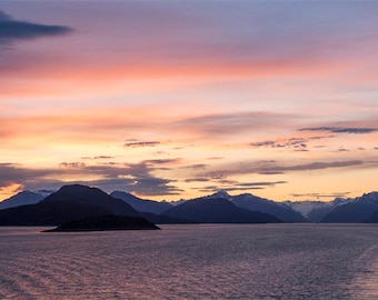 以下が含まれることがあります： 鮮やかな夕焼け空を背景にシルエットになった山脈の風景。山々は湖や湾の穏やかな水面に映り込み、平和で静かな雰囲気を作り出しています。
