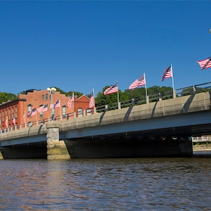 May include: A bridge over a river with a red brick building in the background. The bridge is decorated with American flags.
