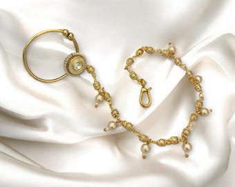 May include: A gold-coloured nose ring with a pearl and crystal centrepiece, linked to a chain of pearls and beads. The jewellery has a hook clasp and is shown on a white satin backdrop.