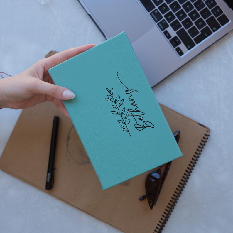 May include: A teal blue notebook with a black floral design and the name "Bethany" written in cursive.