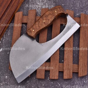 May include: A large, curved cleaver with a wooden handle and a wide, silver blade. The handle is a light brown color with a wood grain pattern and brass rivets. The blade has the text "KnivnBlades" on it.