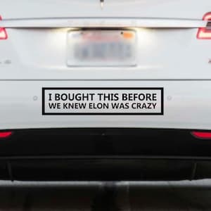 May include: A white Tesla with a black bumper sticker that reads "I bought this before we knew Elon was crazy."