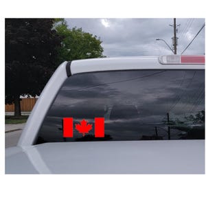 May include: A red Canadian flag decal on the back window of a white pickup truck.
