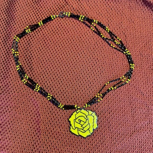 May include: A multi-strand necklace made of black and yellow beads with a yellow beaded rose pendant.