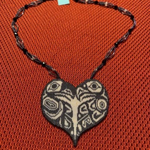 May include: A black and white beaded necklace with a heart-shaped pendant. The pendant features a geometric design with intricate details.