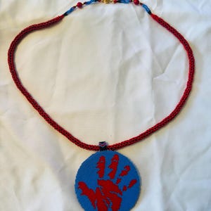 May include: A red beaded necklace with a blue and red beaded pendant featuring a handprint design.