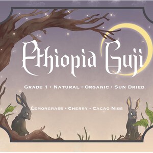 May include: A whimsical illustration of a moonlit forest with two rabbits. The text "Ethiopia Guji" is written in a stylized font. The text "Grade 1 * Natural * Organic * Sun Dried" is written below the title. The text "Lemongrass * Cherry * Cacao Nibs" is written below the rabbits.