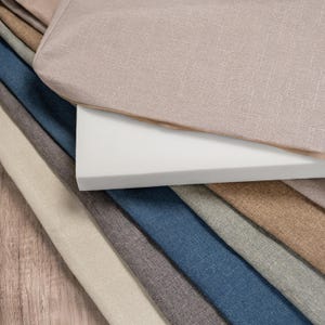 May include: A stack of fabric swatches in various colours and textures, including beige, brown, grey, blue, and white. The swatches are arranged in a fan shape, with the beige fabric on top.