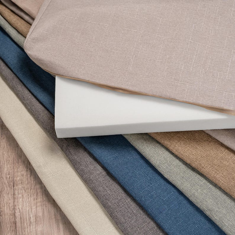 May include: A stack of fabric swatches in various colours and textures, including beige, brown, grey, blue, and white. The swatches are arranged in a fan shape, with the beige fabric on top.