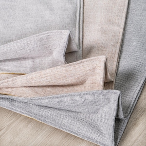 May include: Four fabric swatches in different shades of gray and beige. The swatches are folded and layered on top of each other, with a subtle yellow seam visible along the edges.