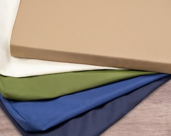 May include: A stack of five fabric cushions in different colors, including beige, white, green, blue, and navy blue. The cushions are arranged in a staggered pattern, with the beige cushion on top.