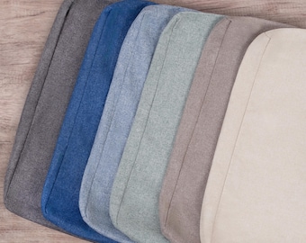 May include: A set of seven fabric chair cushions in various colors, including gray, blue, light blue, green, beige, and cream. The cushions are all the same size and shape, and they are arranged in a row.