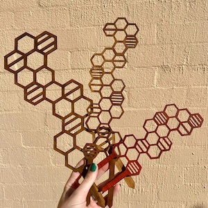 May include: Three metal honeycomb-shaped garden stakes in gold and red. The stakes are held in a hand.
