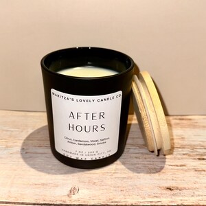 Op de afbeelding: Een matzwarte kaars in een pot met een wit etiket met de tekst MARITZA'S LOVELY CANDLE CO. AFTER HOURS, Citrus, Cardamom, Violet, Saffron, Amber, Sandalwood, Smoke, 7 oz / 200 g, HANDMADE IN UNION CITY, PA, SOY WAX CANDLE, inclusief een licht houten deksel.