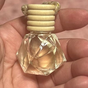 May include: A clear glass bottle with a faceted design, filled with a light-colored liquid. The bottle has a wooden cap with a gold string attached.