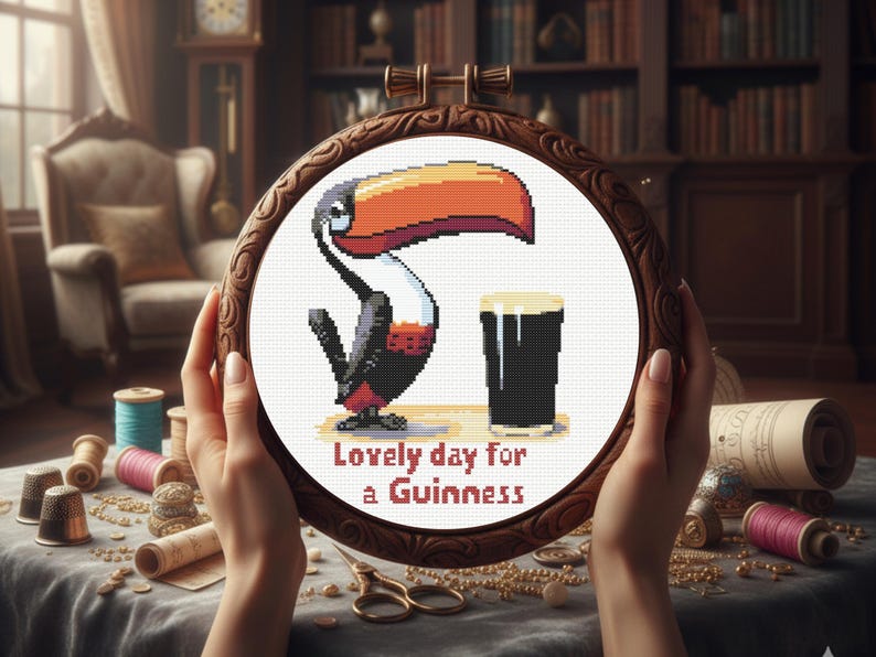 May include: Cross-stitch embroidery in a wooden hoop featuring a toucan and a pint of Guinness. The text "Lovely day for a Guinness" is stitched below the image. The hoop is held by hands, with sewing supplies in the background.