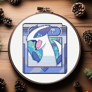 Könnte beinhalten: Kreuzstichmuster eines weißen und blauen Pokémon-Charakters auf einem Game Boy Color-Bildschirm. Der Charakter ist eine weiße, pelzige Kreatur mit blauen Markierungen und einer rosa Nase. Der Game Boy Color-Bildschirm ist blau und grau mit dem Text "TP" in der oberen rechten Ecke.