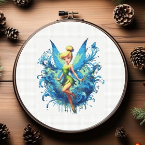 May include: A cross-stitch embroidery hoop with a colorful image of Tinkerbell, a fairy with blue wings and a green dress, surrounded by blue and green floral designs.