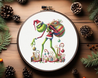 Pode incluir: Um aro de bordado de ponto cruz com um personagem verde do Grinch usando um chapéu de Papai Noel e carregando uma sacola de presentes. O Grinch está cercado por bengalas de doces, enfeites e outras decorações de Natal.