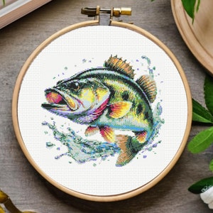 Könnte beinhalten: Eine Kreuzstich-Stickerei eines bunten Barsches, der aus dem Wasser springt. Der Fisch ist grün, gelb, orange und blau. Das Wasser ist blau und weiß.