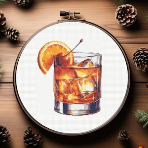 Può includere: Uno schema di punto croce di un cocktail Old Fashioned con una fetta d'arancia e una ciliegia. La bevanda è in un bicchiere di whisky con cubetti di ghiaccio.