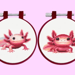 May include: Two pink axolotl cross-stitch patterns on white fabric in red embroidery hoops.
