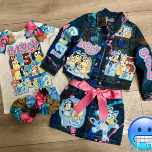 Puede incluir: Una chaqueta vaquera azul con salpicaduras de pintura y parches con personajes del programa de dibujos animados Bluey. La chaqueta tiene las palabras "Bluey", "Laura" y "5" escritas en ella. Una falda vaquera azul con salpicaduras de pintura y parches con personajes del programa de dibujos animados Bluey. La falda tiene las palabras "Bluey" y "Laura" escritas en ella. Una camiseta blanca con las palabras "Bluey", "Laura" y "5" escritas en ella. La camiseta tiene una imagen de los personajes del programa de dibujos animados Bluey.