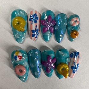 May include: Set of ten blue and white summer themed nail tips with various designs including a pink flower, a yellow duck, a striped life preserver, a starfish, a beach ball, and a pink donut.