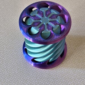 May include: A teal blue and purple 3D printed fidget toy with a spiral design and a starburst pattern on the top.