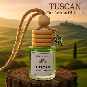 May include: A Tuscan car aroma diffuser with a green liquid in a glass bottle. The bottle has a wooden cap and a decorative leaf charm. The text "TUSCAN Car Aroma Diffuser" is at the top, and "AURA collection by ZEN ART" is on the label.