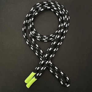 May include: Black and white patterned shoelaces with bright green aglets. The laces are arranged in a figure-eight pattern against a black background. The shoelaces are made of a durable, woven material.