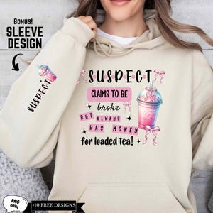 May include: A beige hoodie with a pink and black graphic design that says "SUSPECT CLAIMS TO BE BROKE BUT ALWAYS HAS MONEY FOR LOADED TEA!" with a pink and white cartoon image of a drink with a straw. The sleeve of the hoodie has the word "SUSPECT" written vertically in black.