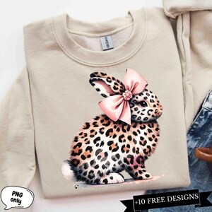 May include: A beige sweatshirt with a graphic of a leopard print bunny wearing a pink bow. The bunny is sitting on a white background.