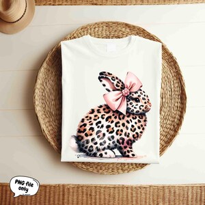 May include: A white t-shirt with a graphic of a leopard print bunny wearing a pink bow.