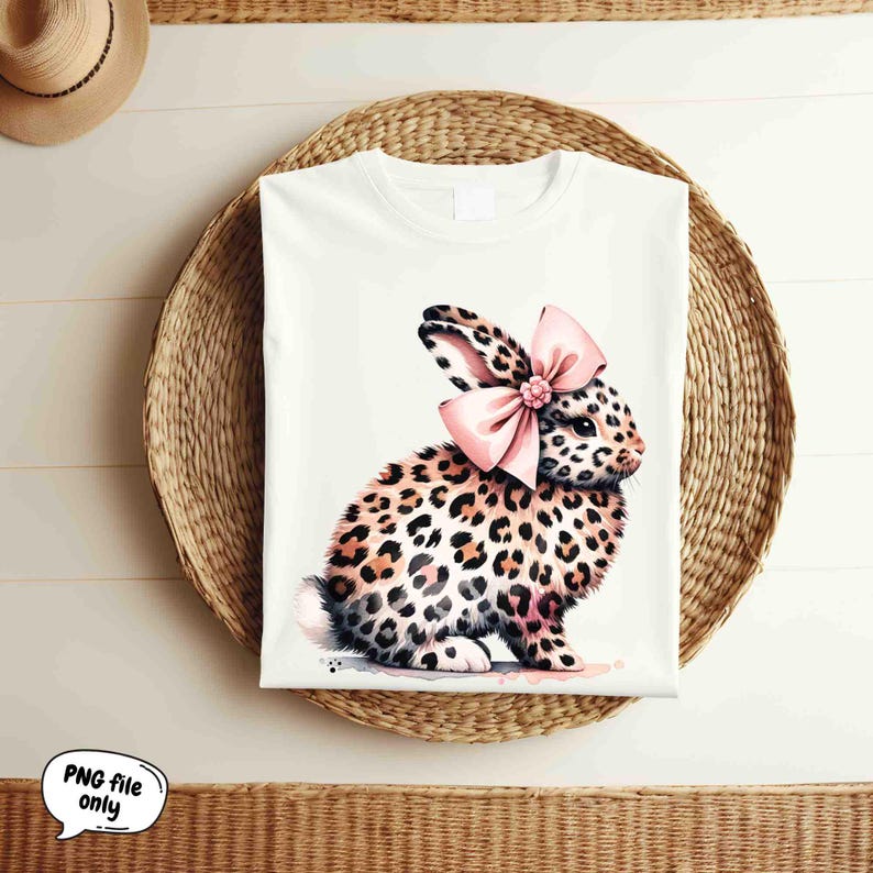May include: A white t-shirt with a graphic of a leopard print bunny wearing a pink bow.