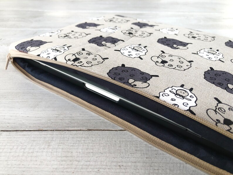 May include: A beige laptop sleeve with a zipper closure. The sleeve is decorated with a repeating pattern of black and white sheep.