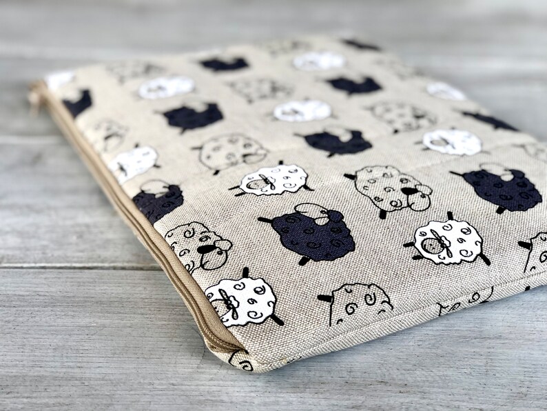 May include: A beige linen zippered pouch with a repeating pattern of black and white sheep. The pouch has a zipper closure and a brown zipper pull.