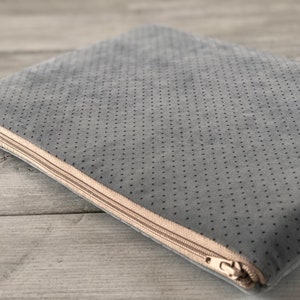May include: A gray laptop sleeve with a dotted pattern and a beige zipper. The sleeve is made of a soft, textured material and is designed to protect a laptop. The zipper runs along the top edge.