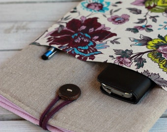 May include: A gray linen pouch with a floral fabric lining. The pouch has a wooden button closure and a pink trim. A black wallet and a blue pen are inside the pouch.