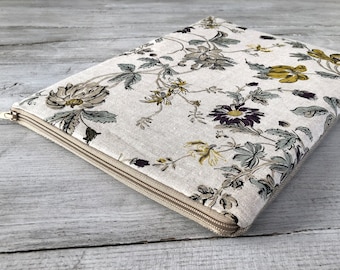 May include: A beige linen zippered pouch with a floral print featuring yellow, green, and purple flowers. The pouch is lying on a light wood surface.