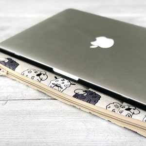 May include: A beige laptop sleeve with a zipper closure and a black and white sheep pattern. A silver laptop is inside the sleeve.