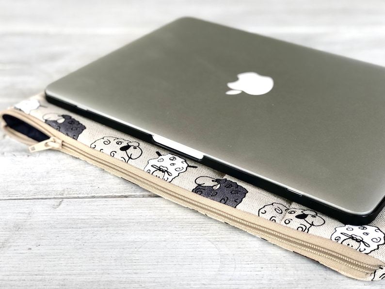 May include: A beige laptop sleeve with a zipper closure and a black and white sheep pattern. A silver laptop is inside the sleeve.
