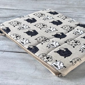 May include: A beige zippered pouch with a repeating pattern of black and white sheep. The pouch is made of a soft, textured fabric.