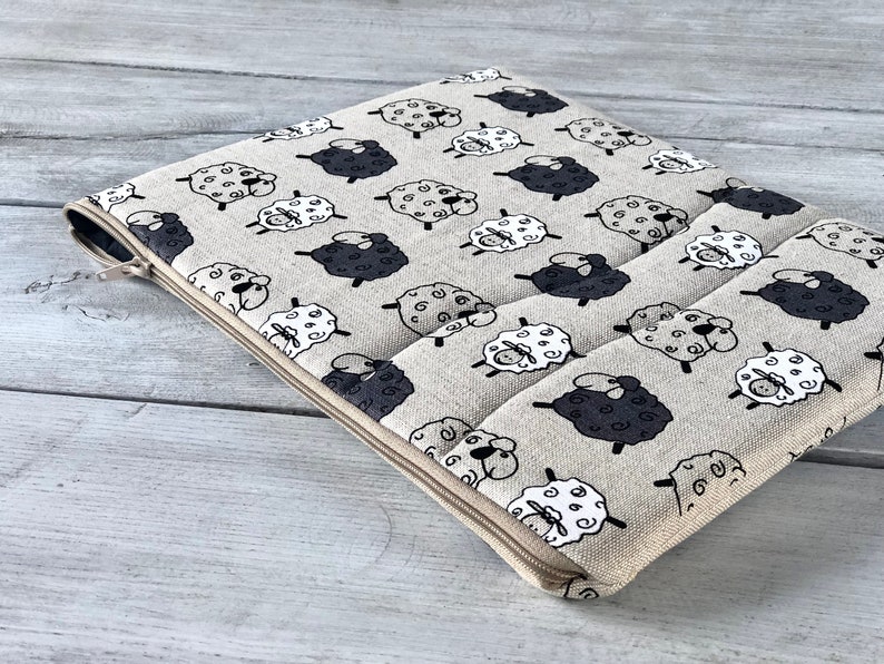 May include: A beige zippered pouch with a repeating pattern of black and white sheep. The pouch is made of a soft, textured fabric.