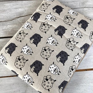 May include: Beige fabric with a repeating pattern of black and white sheep. The sheep are stylized and have curly wool.