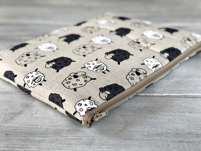 May include: A beige zippered pouch with a black and white sheep pattern. The pouch is made of a soft, textured fabric and has a zipper closure.