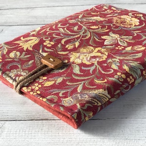 May include: A rectangular case with a floral pattern in red, gold, and green. It features a wooden button and rope closure. The edges are trimmed with red fabric. The case is likely designed to hold items.