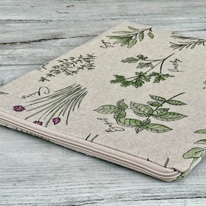 May include: A beige zippered pouch with a white zipper. The pouch is decorated with a pattern of green herbs and the names of the herbs in black lettering. The herbs include chives, parsley, basil, and thyme.