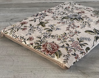 Könnte beinhalten: Eine beige Reißverschlusstasche mit einem Blumenmuster. Das Muster zeigt eine Vielzahl von Blumen in den Farben Rosa, Rot und Grün.