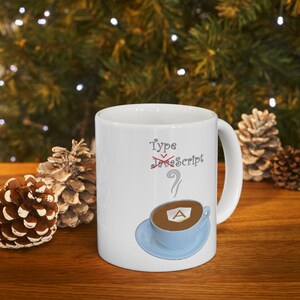 May include: White ceramic mug with the text "Type  JavaScript" with a red line through JavaScript and a question mark. The mug has a blue and white illustration of a coffee cup with a steaming cup of coffee with the letter "A" in the coffee.
